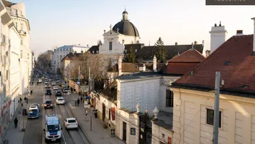 Panoramablick auf eine belebte Stadtstraße mit historischen Gebäuden und einer Kirche im Hintergrund.