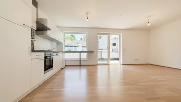 Heller offener Wohn- und Essbereich mit moderner Einbauküche und Zugang zum Balkon.