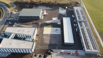 Luftaufnahme eines modernen Gewerbeparks mit mehreren Gebäuden, großen Freiflächen und Photovoltaikanlagen auf den Dächern.