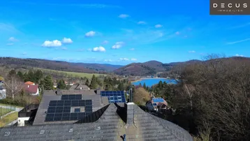 Luftaufnahme eines Hauses mit Solaranlage auf dem Dach und weitem Blick über die Landschaft und einen See.