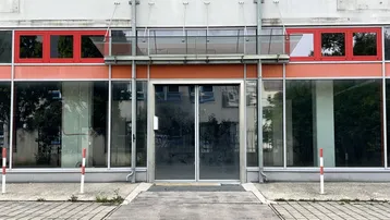 Eingangsbereich eines Geschäftsgebäudes mit großen Glasfronten und roten Fensterrahmen.