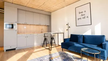 Modernes Studio-Apartment mit integrierter Küchenzeile, Holzboden und gemütlichem blauen Sofa.