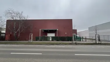 Rote Fassade eines Industriegebäudes mit Zufahrt von der Straße und umzäuntem Bereich.