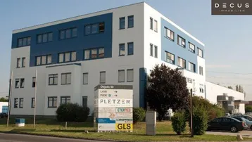 Modernes Bürogebäude mit weißer und blauer Fassade, umgeben von Grünflächen und Parkplätzen, inklusive Firmenschild.