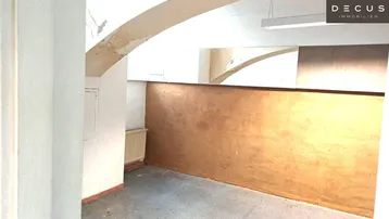 Innenraum mit sichtbaren Bögen, Heizkörper und einer Wand mit abblätternder Farbe, möglicherweise ein Lagerraum.