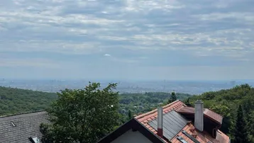 Panoramablick über Dächer und grüne Hügel mit der Stadt in der Ferne.