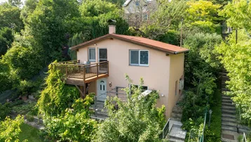 Freistehendes Haus mit Balkon und Garten, umgeben von üppigem Grün in Hanglage.