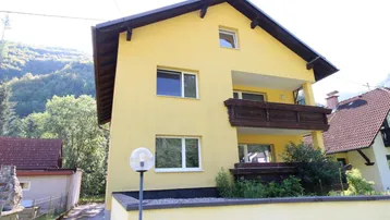 Gelbes Haus mit Holzbalkon und Satteldach in bergiger Umgebung.