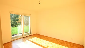 Helles Zimmer mit Parkettboden und Zugang zu einem Balkon, ideal für Wohn- oder Schlafbereich.
