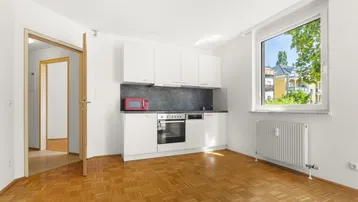 Helle Küchenzeile mit weißen Schränken, Parkettboden und Blick ins Grüne.
