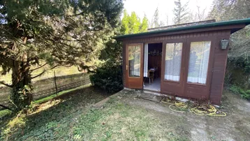 Kleines Holzhaus im Garten mit offener Tür und umgebender Vegetation, ideal als Rückzugsort.