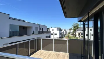 Geräumiger Balkon mit Holzboden und Blick auf moderne Gebäude unter blauem Himmel.