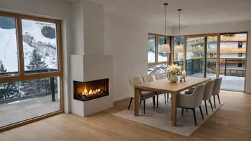 Heller Essbereich mit Holztisch, modernem Kamin und großen Fenstern mit Blick auf die verschneite Landschaft.