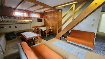 Gemütlicher Wohn- und Essbereich mit Holzvertäfelung, sichtbaren Deckenbalken und Treppenzugang.