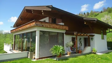Charmantes Haus im alpinen Stil mit Wintergarten und Terrasse, umgeben von grüner Landschaft.
