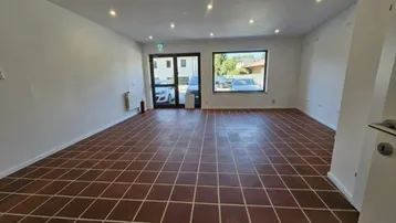 Geräumiger, leerer Geschäftsraum mit Terrakottafliesen und großen Fenstern, die viel Tageslicht hereinlassen.