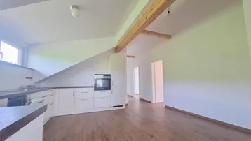 Moderne Küche mit weißen Schränken, Holzboden und sichtbarem Deckenbalken unter Dachschräge.