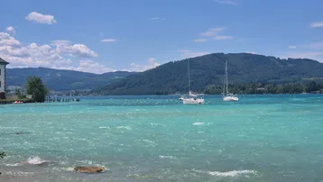 Atemberaubender Blick auf den türkisfarbenen See mit Segelbooten und bewaldeten Bergen im Hintergrund.
