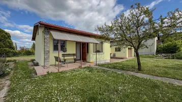 Kleines Einfamilienhaus mit gelber Fassade und Vorgarten unter blauem Himmel.