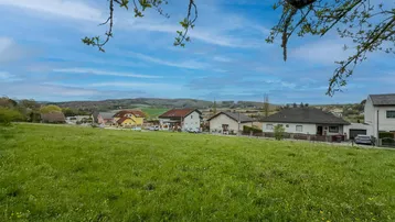 Weitläufige grüne Wiese mit Blick auf die umliegende Wohnbebauung und sanfte Hügel.
