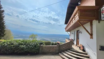 Traditionelles Gebäude mit Holzbalkon und weitem Blick über die Landschaft unter blauem Himmel.