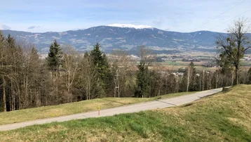 Landschaftsbild mit schneebedeckten Bergen im Hintergrund und einer Straße im Vordergrund.