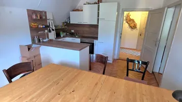 Offener Küchen- und Essbereich mit Holztisch, weißer Küchenzeile und Fischgrätparkett.