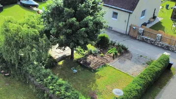 Luftaufnahme eines Einfamilienhauses mit gepflegtem Garten, hohen Hecken und einer Zufahrt.