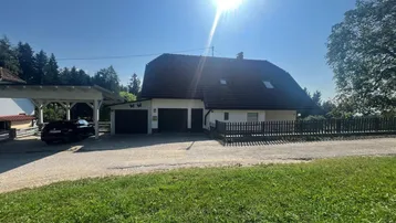 Traditionelles Einfamilienhaus mit Satteldach, Carport und Garage, umgeben von viel Grün.