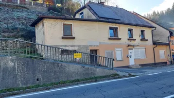 Ansicht eines Hauses an einem Hang mit Solarpaneelen auf dem Dach und einer Straße im Vordergrund.