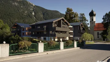 Moderne Architektur im alpinen Stil mit Holzelementen und Blick auf die Berge sowie eine Kirche.