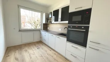 Moderne Küche mit weißen Schränken, Holzakzenten, integrierten Geräten und hellem Holzfußboden.