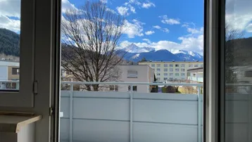 Balkon mit weitem Blick auf die umliegende Berglandschaft und die darunterliegenden Gebäude.