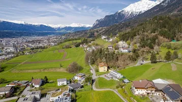 Panoramablick auf die Stadt und die umliegende Berglandschaft unter blauem Himmel.