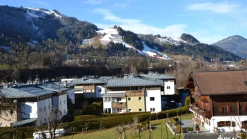 Panoramablick auf Wohngebäude in einer alpinen Landschaft mit schneebedeckten Bergen und Skipisten im Hintergrund.
