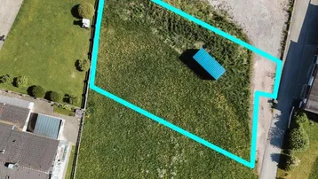 Luftaufnahme eines Grundstücks mit blauer Umrandung, umgeben von Häusern und Grünflächen.