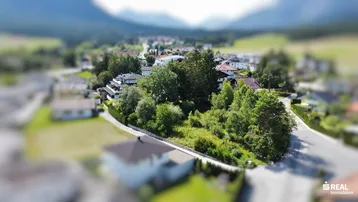 Luftaufnahme eines großen grünen Grundstücks in einer Wohngegend mit Bergkulisse.