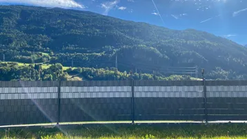 Weitläufiger Blick auf die umliegende Berglandschaft und grüne Natur unter blauem Himmel.