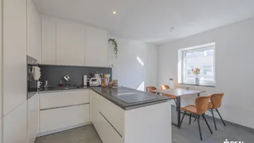 Moderne Küche mit weißen Schränken, dunkler Arbeitsplatte und Essbereich am Fenster.