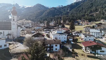 Panoramablick auf ein malerisches Dorf in den Alpen mit traditionellen Häusern und einer Kirche.