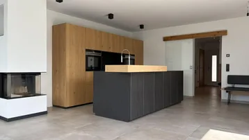 Offener Wohn-Essbereich mit moderner Küche, Kamin und Fliesenboden.