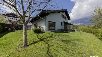 Großzügiger Gartenbereich mit Rasenfläche und Baumbestand vor dem Haus mit Bergblick.