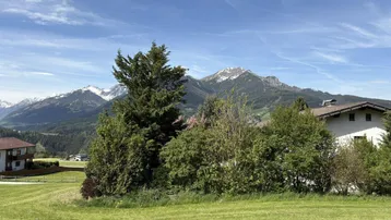 Weitläufige grüne Wiesen und Bäume mit einem atemberaubenden Blick auf schneebedeckte Berge unter blauem Himmel.