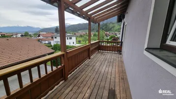 Überdachter Balkon mit Holzboden und schöner Aussicht auf die Berge und Umgebung.