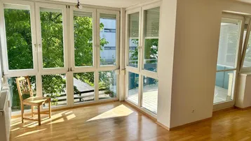 Helles Wohnzimmer mit großen Fenstern, Holzboden und Blick ins Grüne.