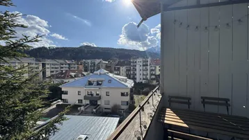 Sonniger Balkon mit Holztisch und Stühlen, bietet einen weiten Blick auf die Stadt und Berge.