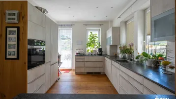 Helle Küche mit Holzfußboden, modernen grauen Schränken und viel Tageslicht durch große Fenster.
