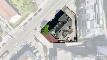 Luftaufnahme eines historischen Gebäudes mit Satteldach und Parkplätzen in städtischer Umgebung.