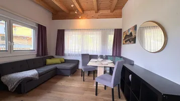 Heller Wohn-Essbereich mit Holzbalkendecke, gemütlichem Sofa und Esstisch auf Holzparkett.