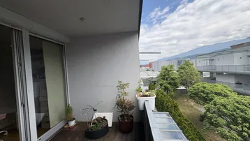 Balkon mit Holzboden, Pflanzen und weitem Blick auf die Berge und die Umgebung.